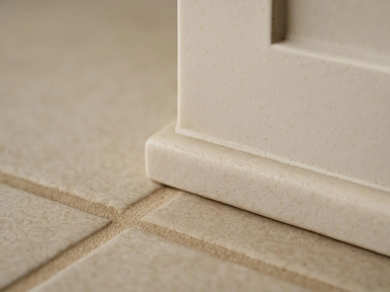 Close-up of a cream cabinet base resting on beige tiled floor with grout lines
