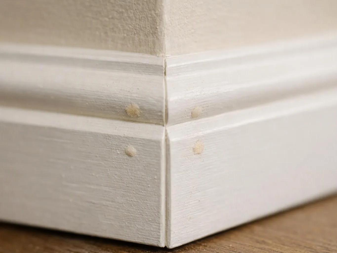 Close-up of a white painted wooden corner with small nail holes on a wood floor