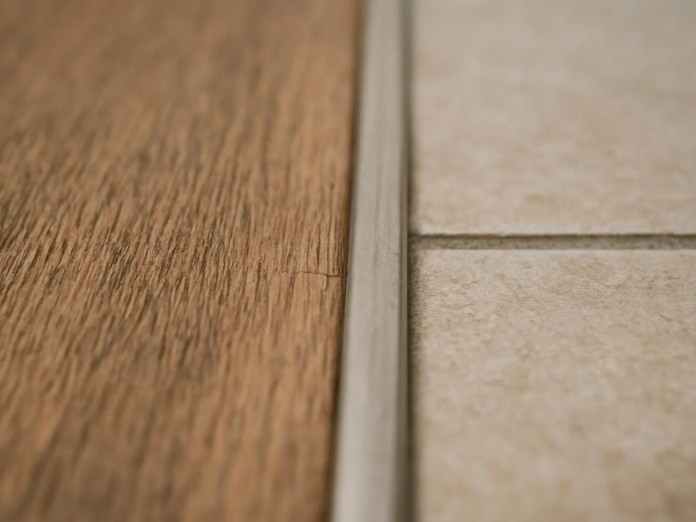 Close-up of a wood floor meeting beige tile with a thin metal transition strip