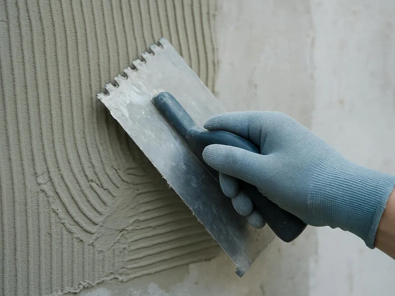 A gloved hand spreads gray mortar on a wall with a notched trowel